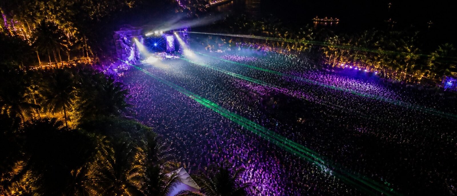 Outdoor electronic music festival at night in Thailand with lasers and palm trees