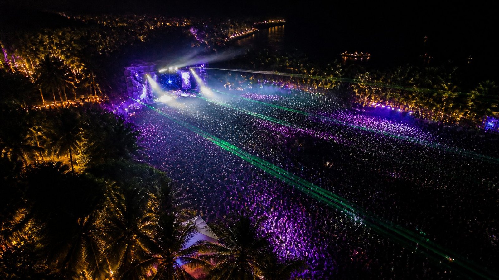 Outdoor electronic music festival at night in Thailand with lasers and palm trees